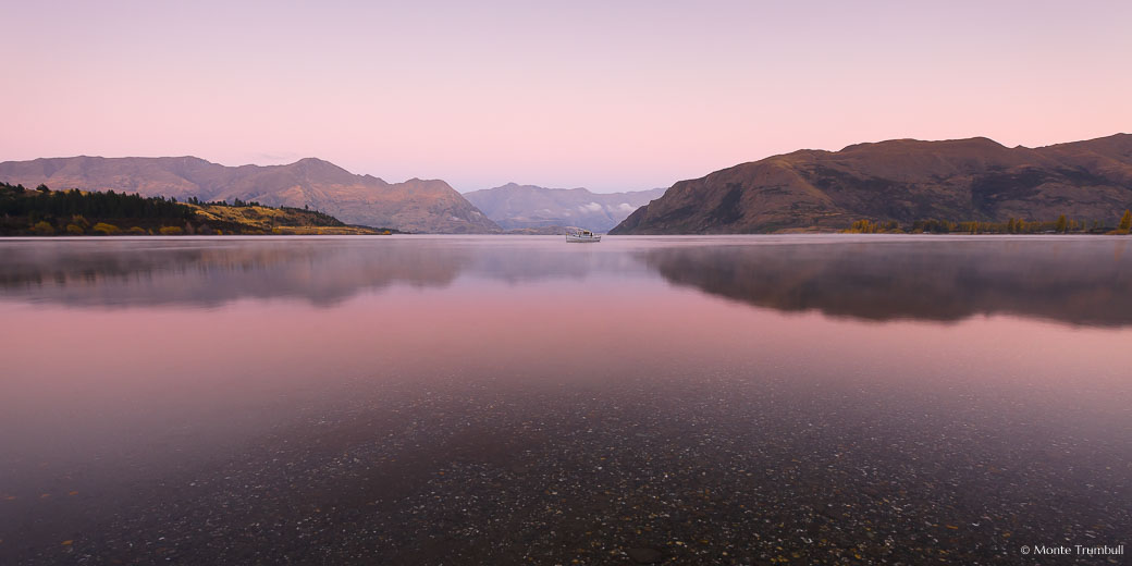 Predawn light bathes Lake Wanaka with soft pink light outside of Wanaka in New Zealand.