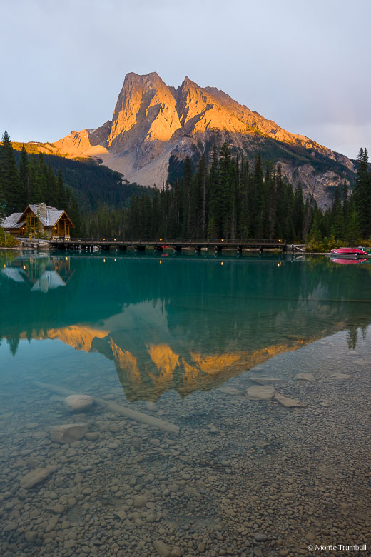The setting sun breaks through the clouds and shines on Mt. Burgess reflected in Emerald Lake in Yoho National Park, Canada.