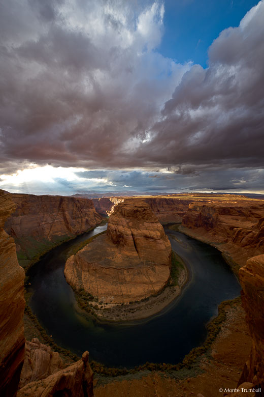 The sun breaks through foreboding storm clouds and lights the walls of the canyon at Horseshoe Bend outside of Page, Arizona.