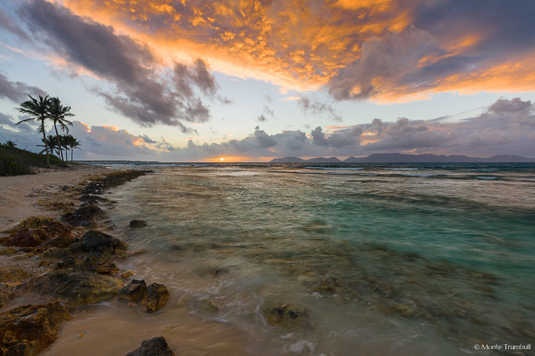The clouds take on an orange glow as the sun rises above the horizon at Merrywing Bay in Anguilla, BWI.