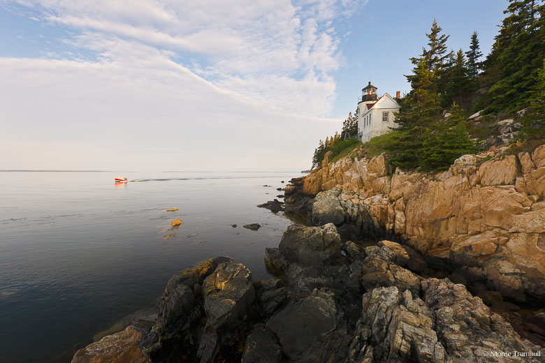 A bright red lobster boat cruises by the Bass Harbor Head Light shortly after sunrise in Acadia National Park, Maine.