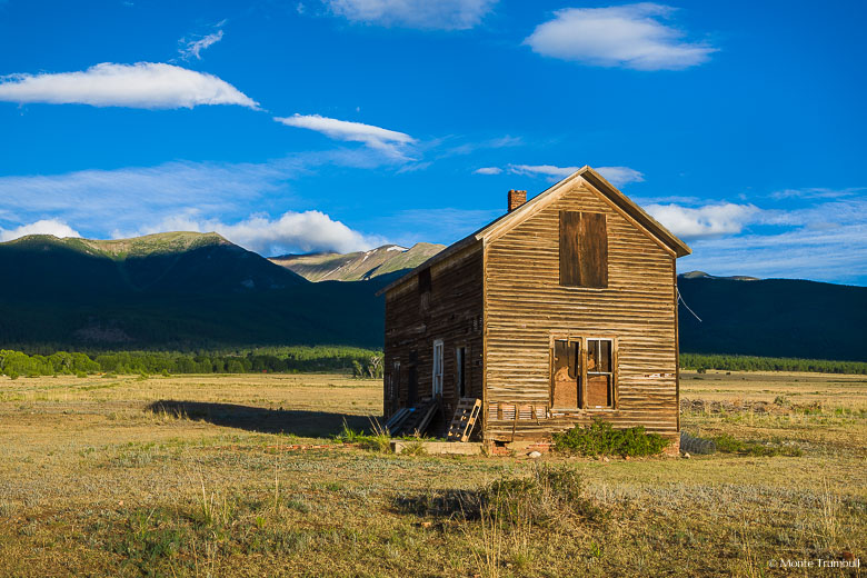 A weathered old house illuminated by early morning light stands out against shadowed mountain peaks outside of Buena Vista, Colorado.