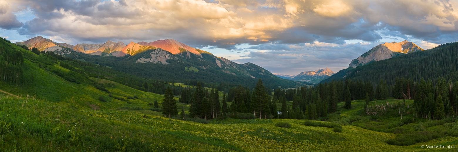 Dorothy Peak, Avery Peak, Crested Butte, and Gothic Mountain are lit by sunlight streaming through glowing clouds at sunset in this panoramic springtime scene looking down the East River Valley outside of Crested Butte, Colorado.