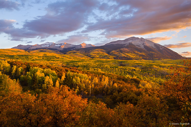 The Beckwith Mountains catch rays from the setting sun behind a valley filled with autumn colors outside of Crested Butte, Colorado.