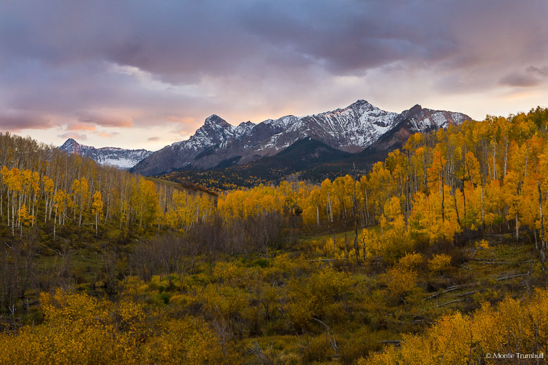 A fall scene in southwestern Colorado with a setting sun illuminating breaking cloud cover over the Sneffels Range outside of Ridgway.