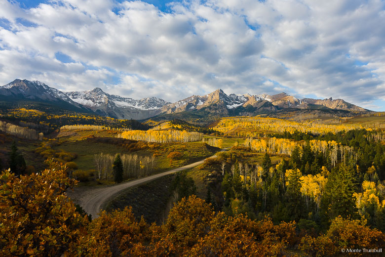 Early morning cloud cover breaks and sunshine spills into a valley filled with golden aspens beneath the Sneffels Range outside of Ridgway, Colorado.