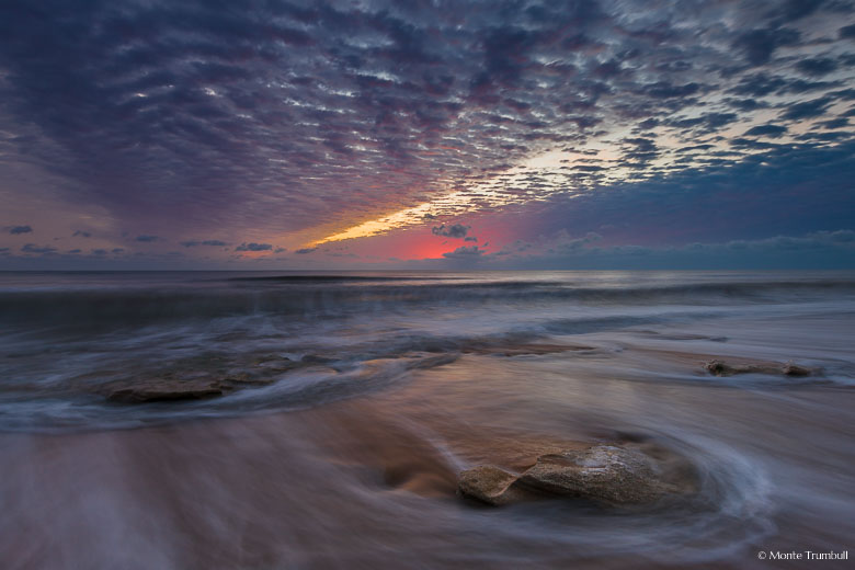 The horizon glows in pink dawn light over a rocky beach at Washington Oaks Gardens State Park, Florida.