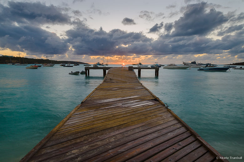 The setting sun glows on the horizon off the end of a pier in Road Bay, Anguilla.
