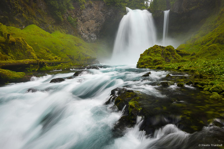 The McKenzie River crashes over Sahalie Falls sending off a cloud of mist in its powerful rush downstream through a vibrant green gorge in the Willamette National Forest in Oregon.