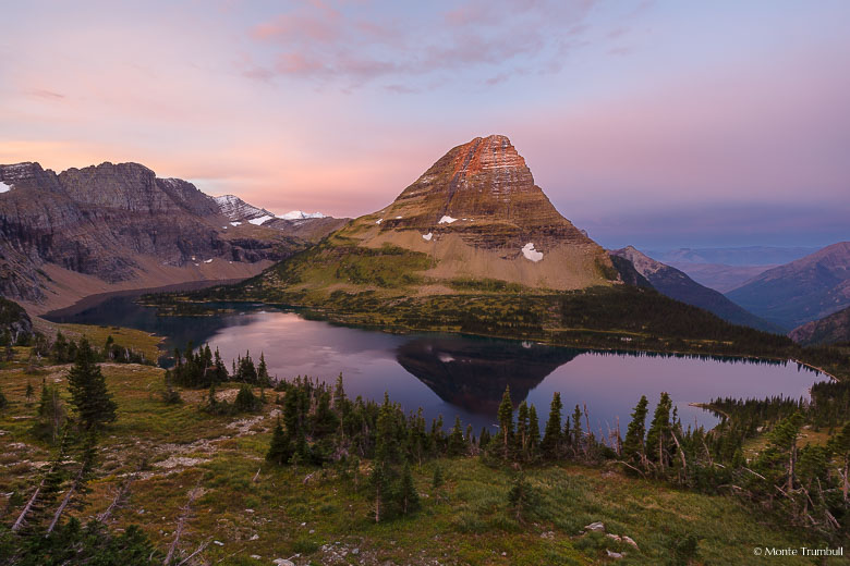 Pink skies surround Bearhat Mountain as it basks in the first light of dawn and is reflected in the waters of Hidden Lake high up in the mountains of Glacier National Park in Montana.