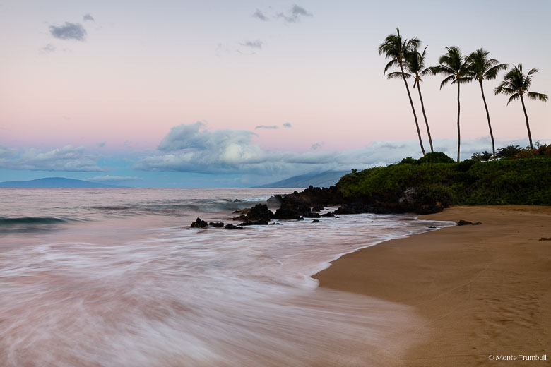 Pink skies at daybreak illuminate the gently breaking waves along the shore of Polo Beach in Maui, Hawaii.