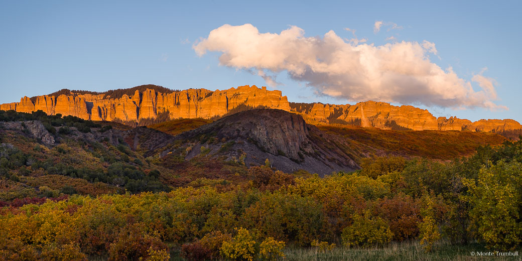 The fleeting autumn rays of the setting sun light up the face of a section of the Cimarron Ridge behind a valley filled with multi-colored brush outside Ridgway, Colorado.