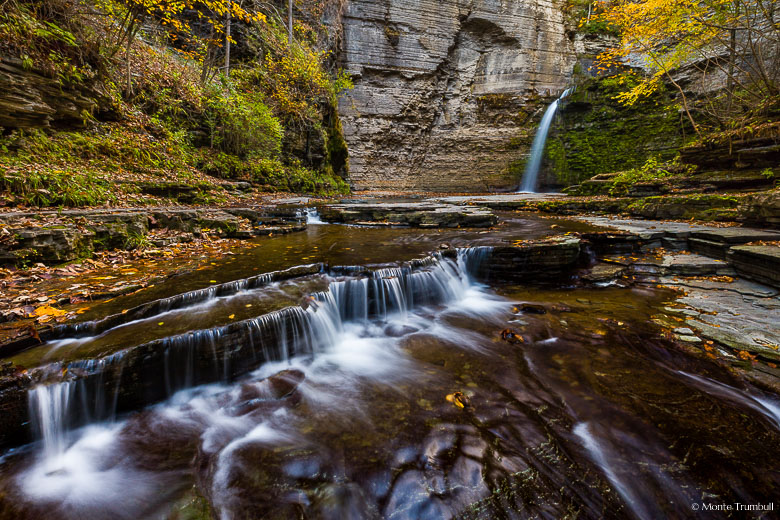 McClure Creek plunges over Eagle Cliff Falls and then over a series of rocky shelves in a narrow, rocky canyon sprinkled with autumn leaves in Havana Glen Park outside of Montour Falls, New York.