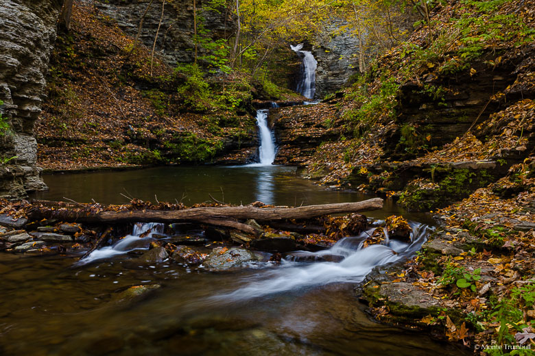 Catlin Mills Creek gently flows over Deckertown Falls and winds its way down to a calm pool ringed with fallen autumn leaves in the village of Montour Falls, New York.