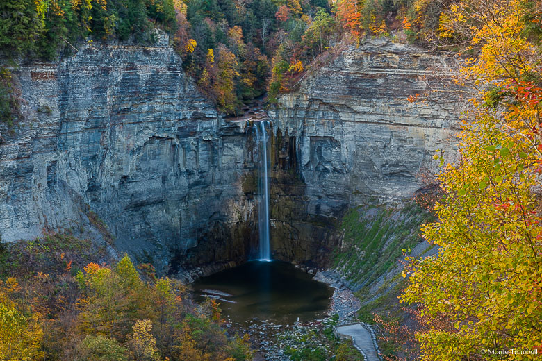 Multicolored trees and brush frame Taughannock Falls as it plunges 215 feet over a rocky cliff into a placid pool at Taughannock Falls State Park in central New York.