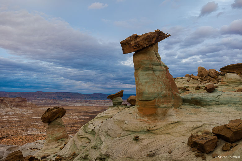 A group of stone hoodoos perched along Stud Horse Point overlook a desert valley below with foreboding evening skies overhead outside of Page, Arizona.