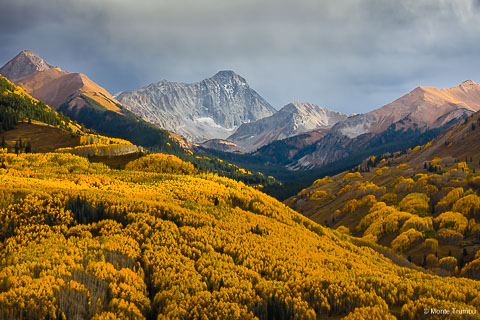 The sun breaks through evening storm clouds and illuminates a valley carpeted in golden aspen trees beneath Capitol Peak outside of Snowmass, Colorado.
